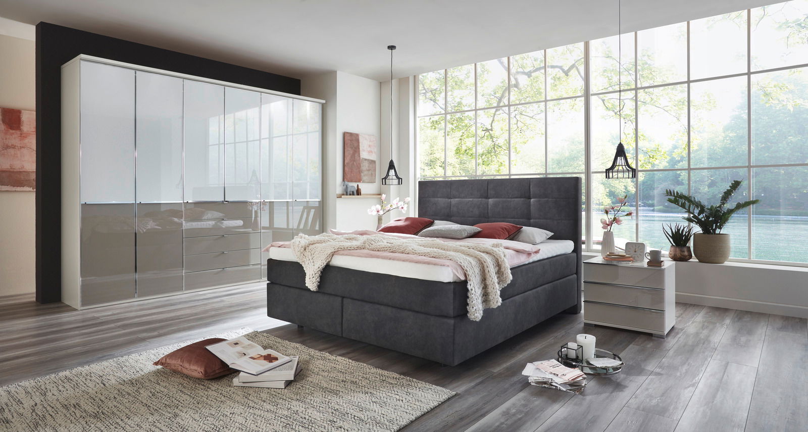 Modernes Boxspringbett in einem stilvollen Schlafzimmer mit großen Fenstern, seitliche Perspektive.