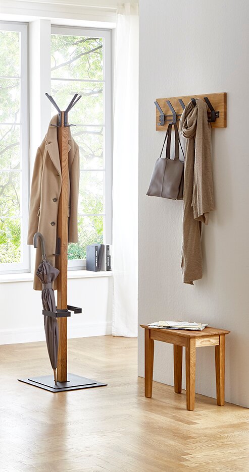 Moderner Garderobenständer aus Holz mit schwarzem Metallfuß und Haken, daneben Wandgarderobe mit Taschen und Schal in hellem Flur; Perspektive: frontale, leicht seitliche Raumansicht