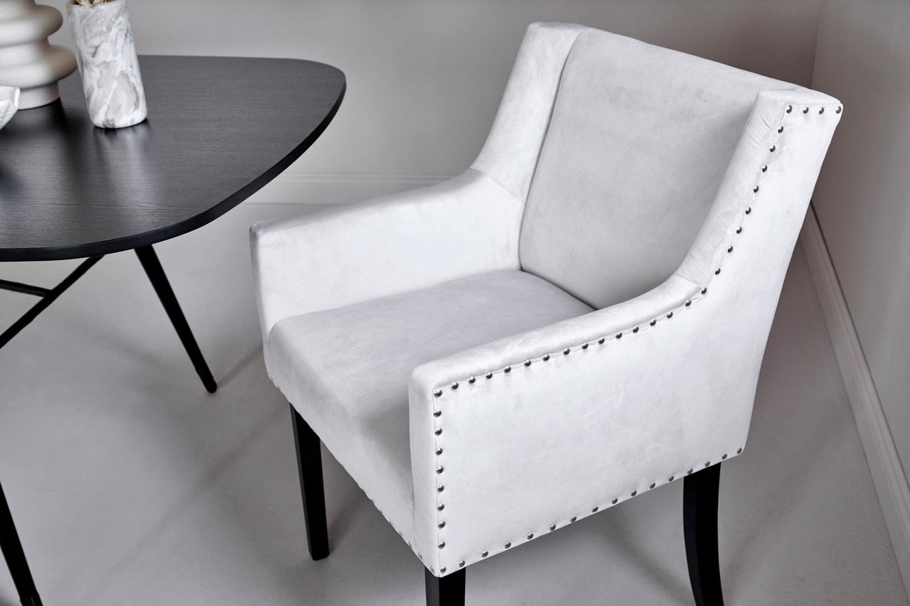 Weißer Polsterstuhl mit Nieten an den Armlehnen, seitliche Perspektive neben einem dunklen Tisch.