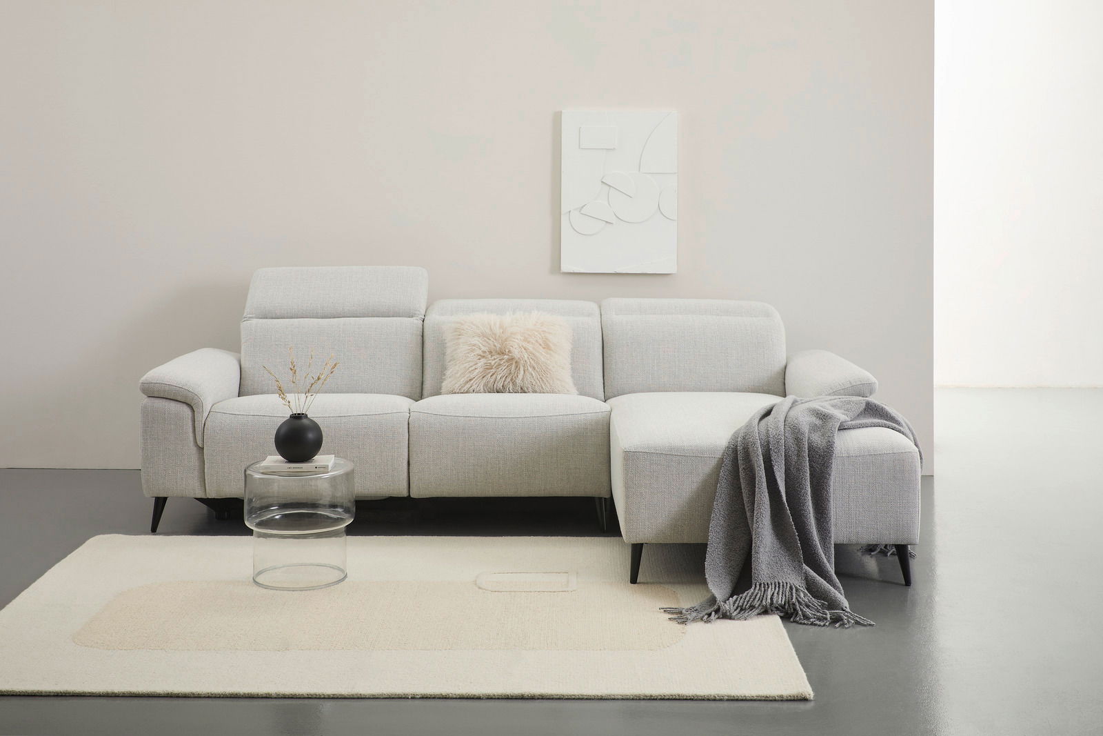 Graue Longchairkombination mit Kissen und Decke, frontal fotografiert, auf einem hellen Teppich mit einem kleinen Tisch und Vase.