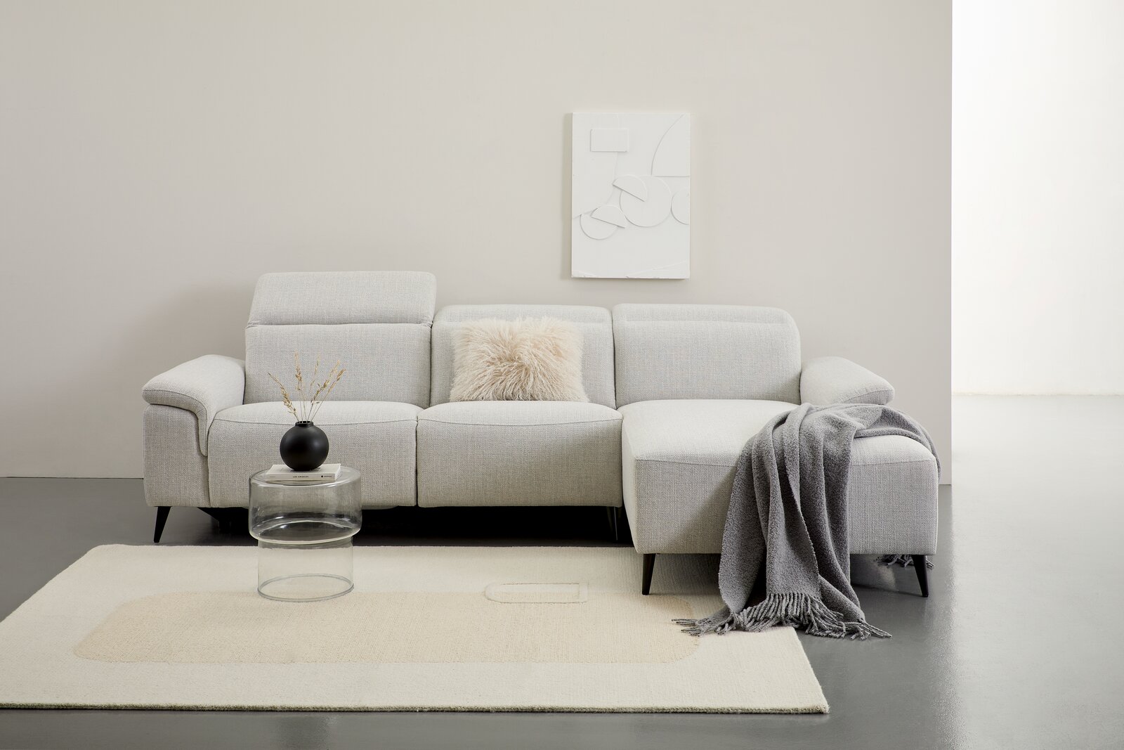 Graue Longchairkombination mit Kissen und Decke, frontal fotografiert, auf einem hellen Teppich mit einem kleinen Tisch und Vase.