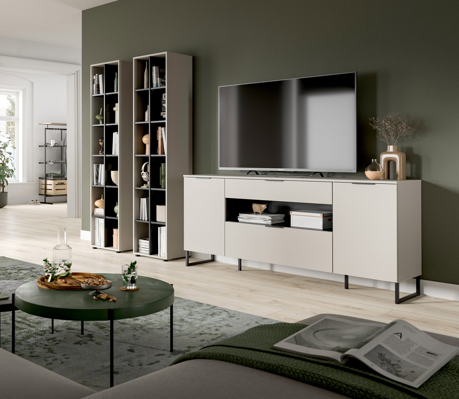 Modernes Wohnzimmer-Setup mit hellem TV-Lowboard auf schwarzen Metallfüßen und großem Flachbildfernseher, daneben zwei hohe offene Regale; Ansicht schräg von vorne aus dem Wohnbereich.
