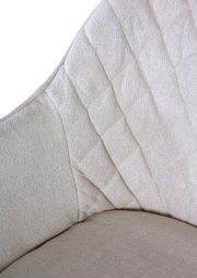 Nahaufnahme eines beigen Armlehnstuhls mit gestepptem Stoffmuster, seitliche Perspektive