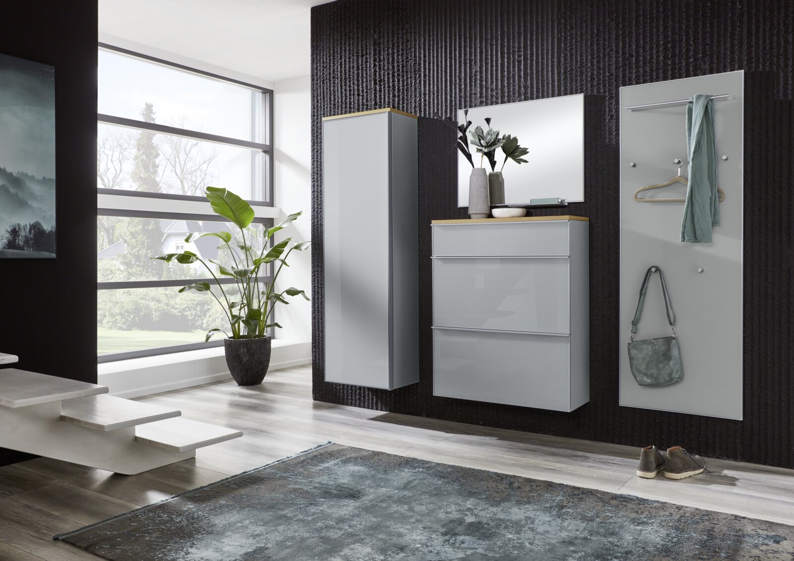 Modernes Garderoben-Set in Hellgrau mit Hochschrank, Schuhschrank und Spiegel sowie Garderobenpaneel mit Haken und Kleiderstange, frontal in leichter Schrägansicht im Flur vor dunkler Wand