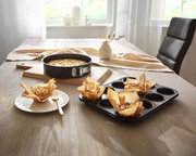 Springform 26 cm auf einem Tisch mit gebackenem Kuchen, umgeben von Muffins in einer Muffinform, seitliche Perspektive