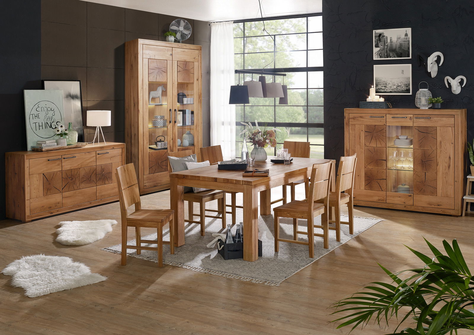 Landscape Highboard I-R MERAN Esszimmer mit Holzmöbeln, bestehend aus einem großen Esstisch mit sechs Stühlen, einem Sideboard, einem Highboard und einer Vitrine. Die Möbel sind aus hellem Holz mit dekorativen Mustern. Im Hintergrund sind große Fenster und eine moderne Wanddekoration