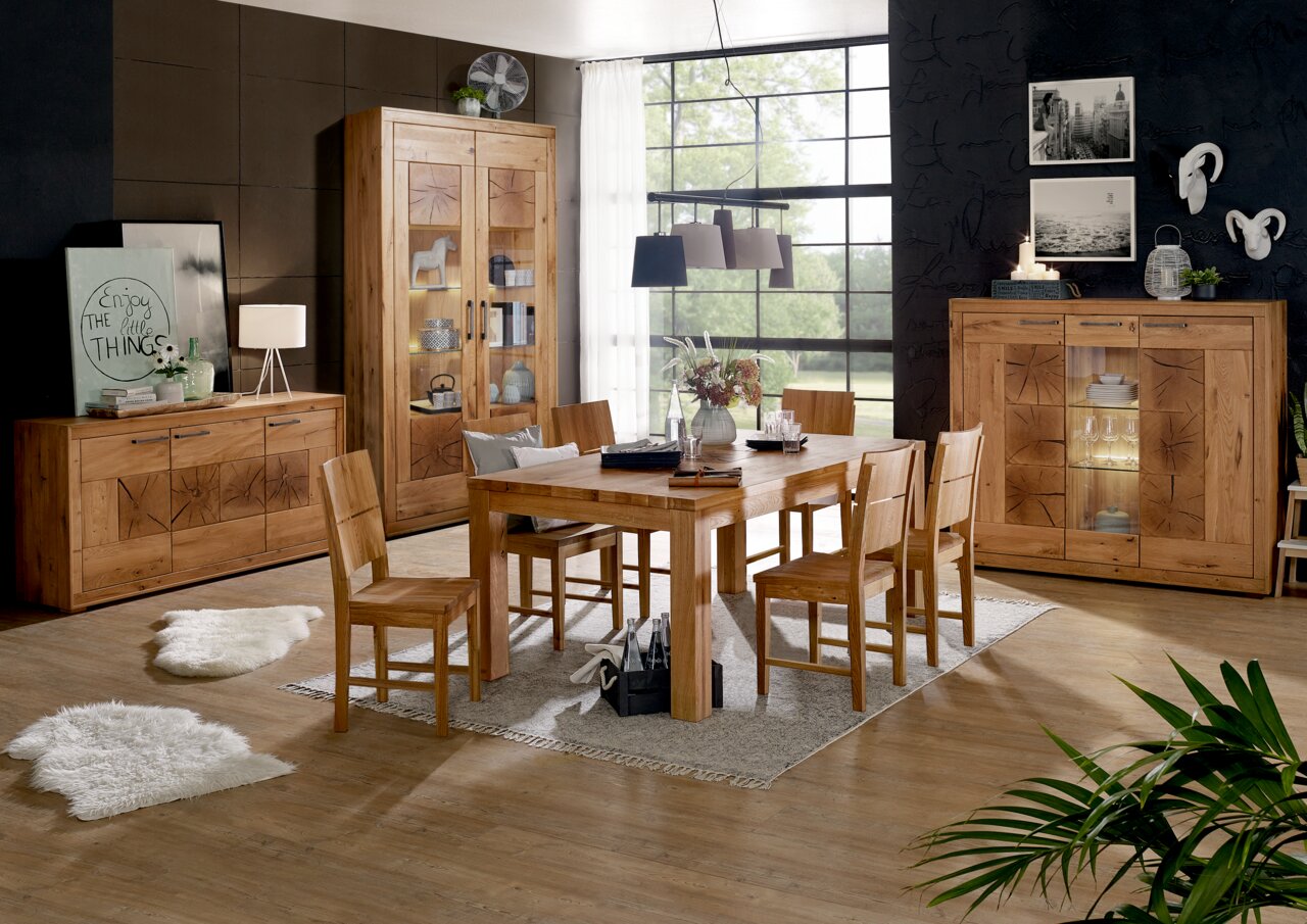 Landscape Highboard I-R MERAN Esszimmer mit Holzmöbeln, bestehend aus einem großen Esstisch mit sechs Stühlen, einem Sideboard, einem Highboard und einer Vitrine. Die Möbel sind aus hellem Holz mit dekorativen Mustern. Im Hintergrund sind große Fenster und eine moderne Wanddekoration