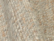 Nahaufnahme eines handgewebten Teppichs mit grober Textur in natürlichen Beige- und Grautönen, seitliche Perspektive