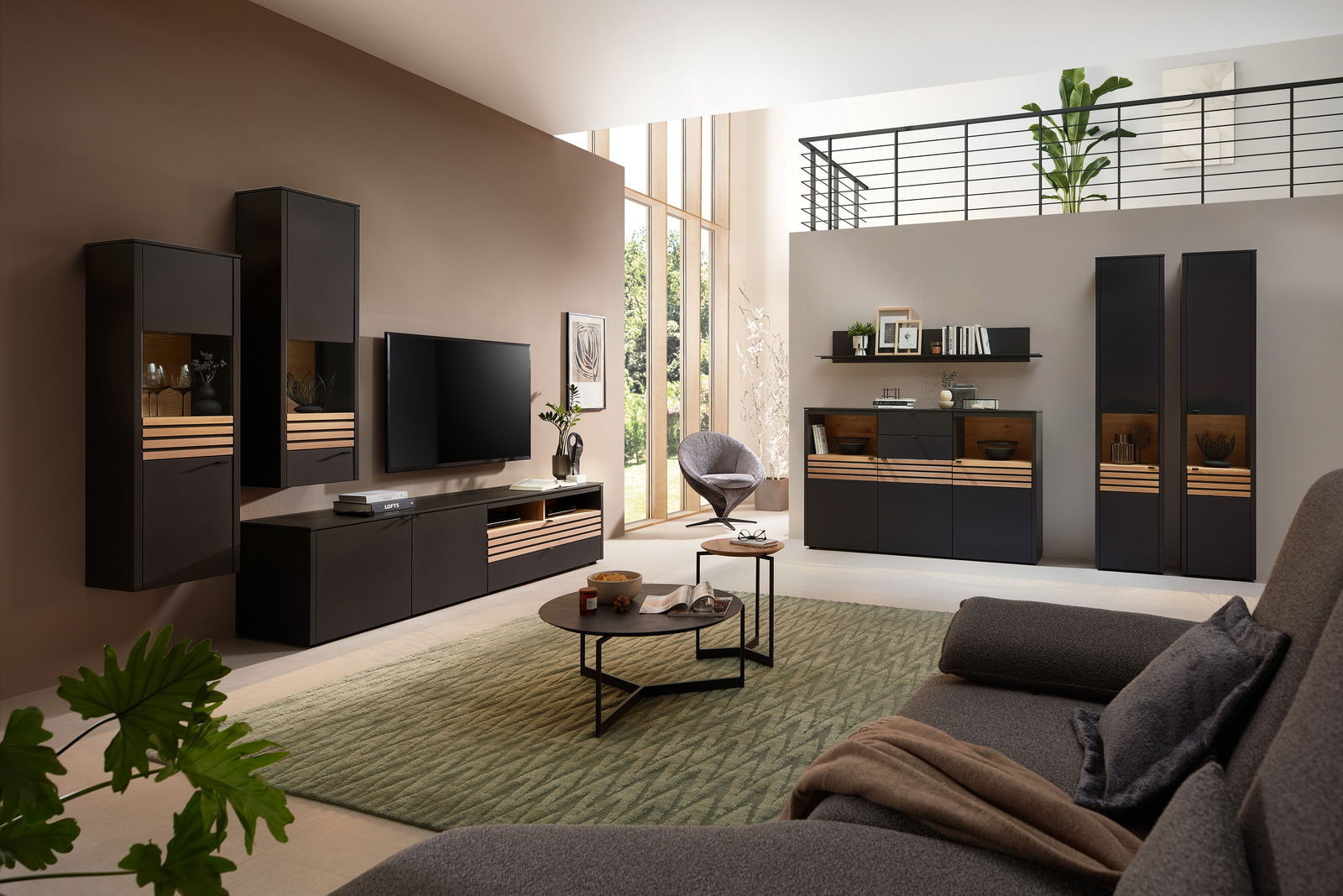 Moderne Wohnzimmer-Wandkombination in dunklen Tönen mit Holzakzenten, bestehend aus Hängeschränken, TV-Board und Vitrine, aus der Perspektive eines gemütlichen Wohnzimmers mit Sofa und Teppich.