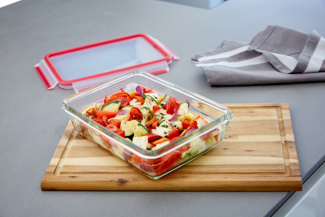 Emsa Frischhaltedose CLIP & CLOSE Rechteckige Glasform mit rotem Deckel, gefüllt mit frischem Salat, auf einem Holzbrett in einer modernen Küche. Perspektive von schräg oben.
