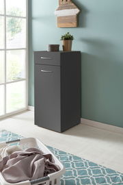 Graue Wäschekommode mit Schublade und Tür, dekoriert mit Pflanze und Dose, in einem hellen Raum mit Fenster, aus seitlicher Perspektive.