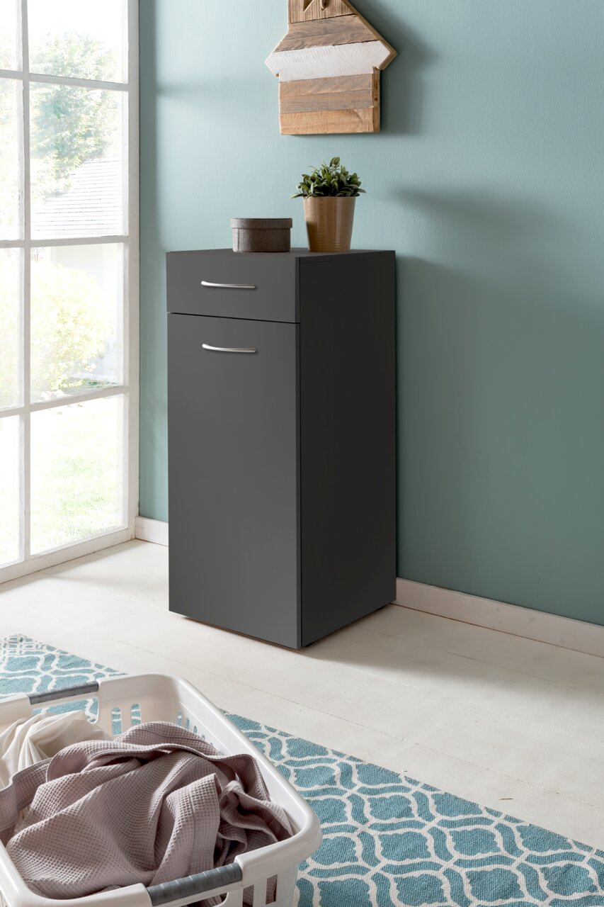 XORA Wäschekommode MULTIRAUMKONZEPT Graue Wäschekommode mit Schublade und Tür, dekoriert mit Pflanze und Dose, in einem hellen Raum mit Fenster, aus seitlicher Perspektive.