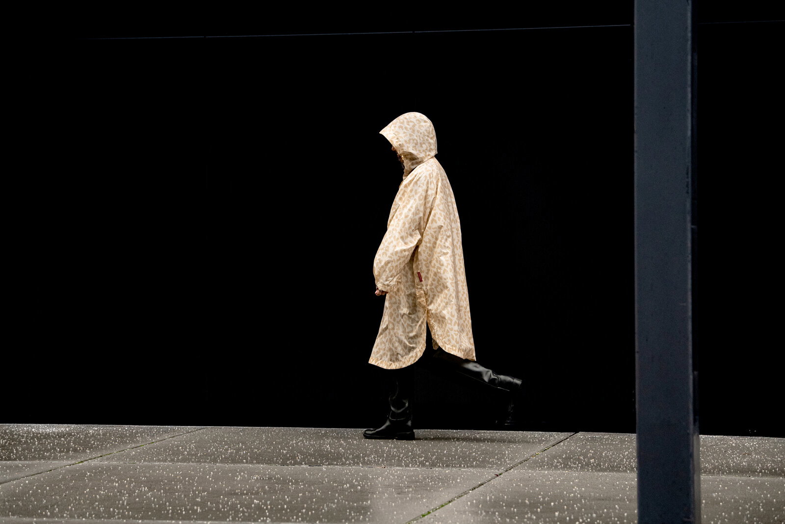 Beiger Regenmantel mit Kapuze und dezentem Leopardenmuster, seitliche Ansicht (Profil) an einer Person vor schwarzem Hintergrund.