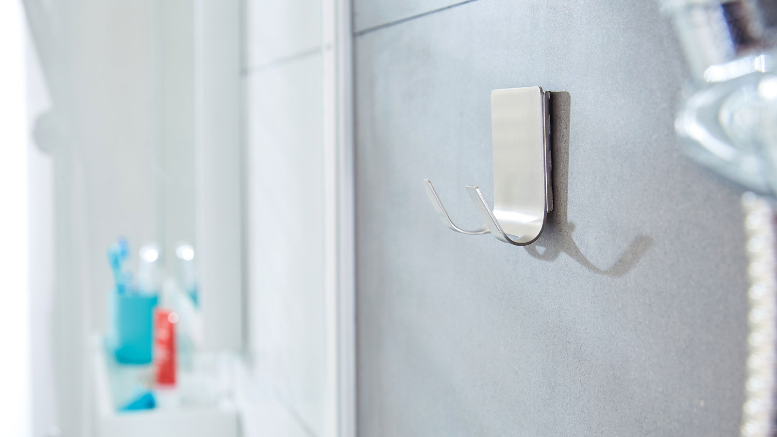 Nahaufnahme eines an der Badezimmerwand befestigten, wasserfesten tesa Powerstrips Hakens aus Metall mit zwei Haken, seitliche Perspektive.