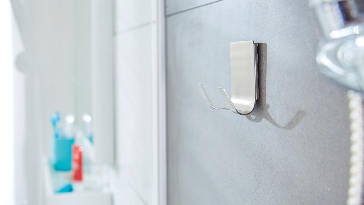 Nahaufnahme eines an der Badezimmerwand befestigten, wasserfesten tesa Powerstrips Hakens aus Metall mit zwei Haken, seitliche Perspektive.