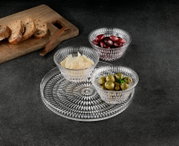 Drie geribbelde glazen schalen met olijven, kaasvlokken en rode olijven op een decoratieve glazen schaal, daarnaast een houten plank met sneetjes brood; perspectief: licht van bovenaf in schuin aanzicht