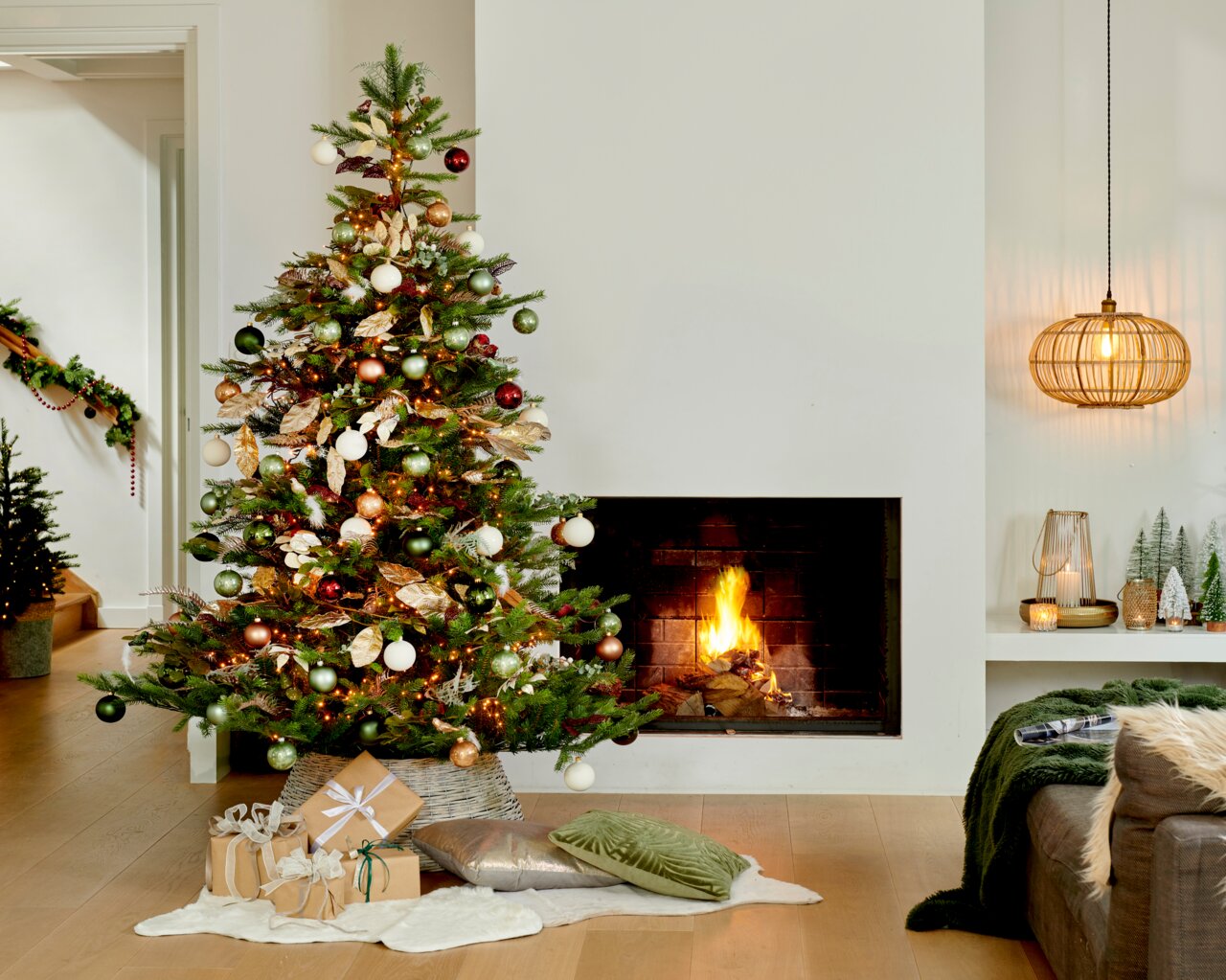Weihnachtsbaum mit bunten Kugeln und Lichtern, neben einem brennenden Kamin, aus der Frontalperspektive fotografiert.