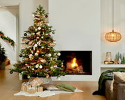 Weihnachtsbaum mit bunten Kugeln und Lichtern, neben einem brennenden Kamin, aus der Frontalperspektive fotografiert.