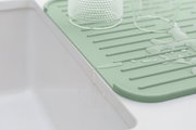 Grüne Silikon Abtropfmatte neben einem Waschbecken, mit Wasser und Gläsern darauf, aus seitlicher Perspektive.