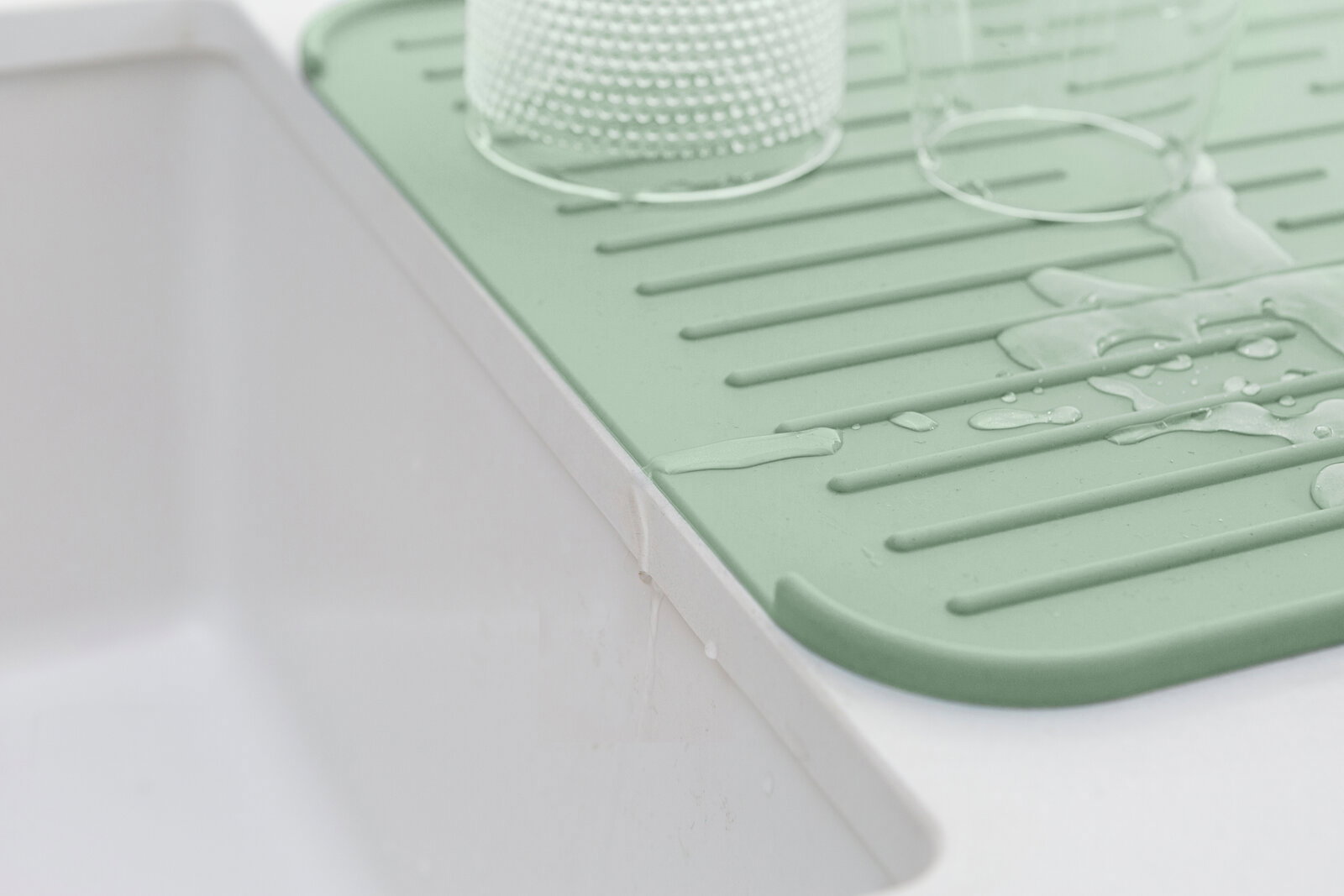 Grüne Silikon Abtropfmatte neben einem Waschbecken, mit Wasser und Gläsern darauf, aus seitlicher Perspektive.
