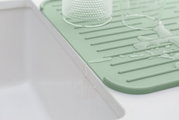 Grüne Silikon Abtropfmatte neben einem Waschbecken, mit Wasser und Gläsern darauf, aus seitlicher Perspektive.