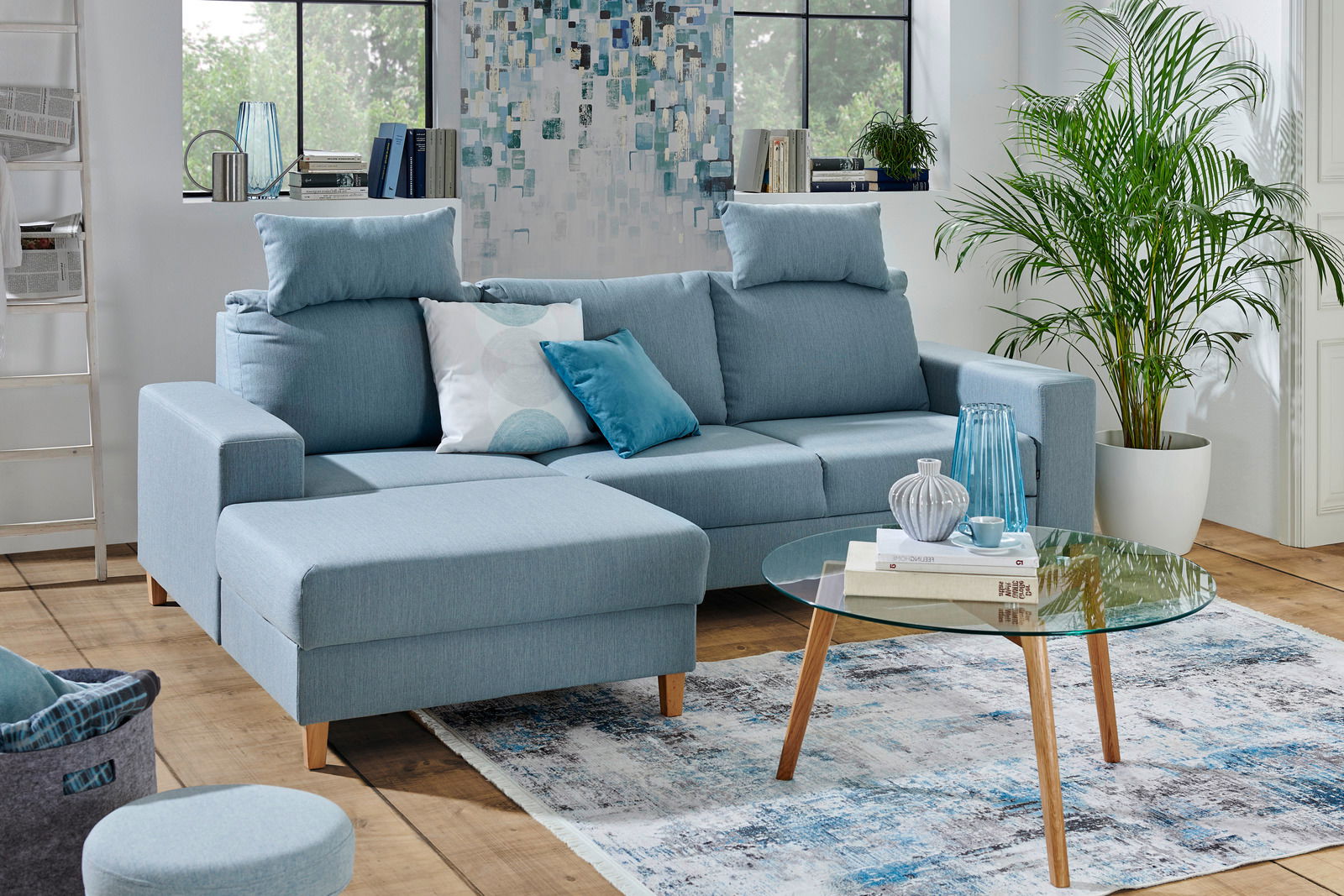 Ti´me Ecksofa ANABELLE Blaue Ecksofa Rundecke Ottli in einem modernen Wohnzimmer, mit Kissen dekoriert, aus der Vorderansicht fotografiert.