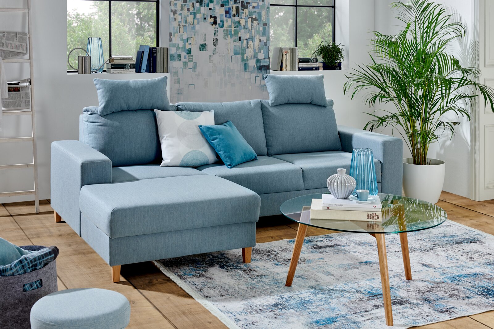Blaue Ecksofa Rundecke Ottli in einem modernen Wohnzimmer, mit Kissen dekoriert, aus der Vorderansicht fotografiert.