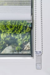 Doppelrollo mit Blende, teilweise heruntergelassen, an einem Fenster montiert, mit Blick auf einen grünen Garten im Hintergrund.