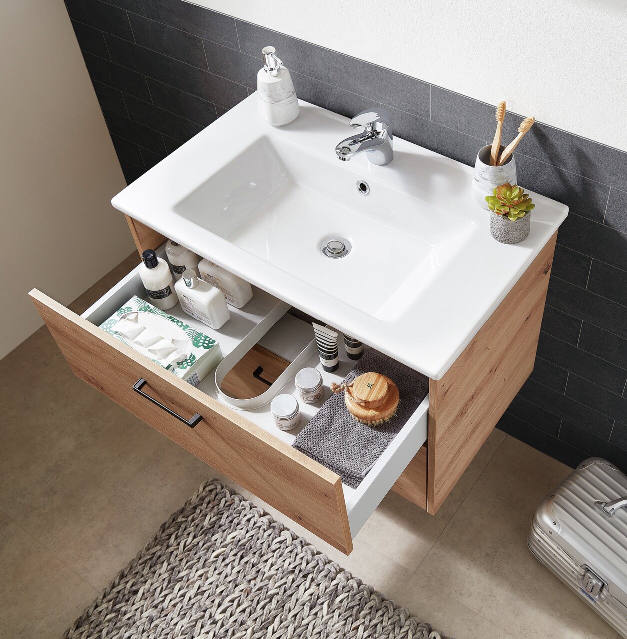 XORA Waschtischunterschrank XO1000 Moderner Waschtischunterschrank aus Holz mit geöffneter Schublade, gefüllt mit Pflegeprodukten, von oben betrachtet.