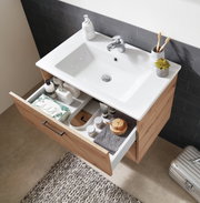 Moderne houten wastafelonderkast met een open lade, gevuld met verzorgingsproducten, gezien van bovenaf.