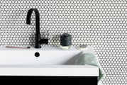 Moderne zeepdispenser op een wastafel met een zwarte kraan, op de achtergrond een muur met een cirkelvormig patroon, zijaanzicht.