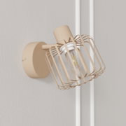 Beige Wandlampe im Industrial-Design mit rechteckigem Drahtgitter-Schirm und sichtbarer LED-Glühbirne, schräg von vorne aus leichter Untersicht an der Wand fotografiert.