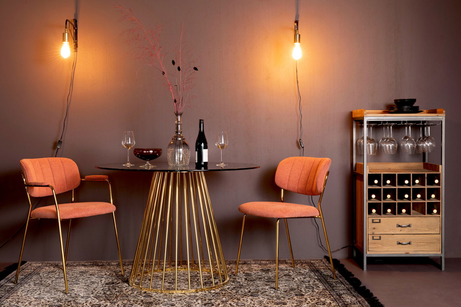 Z2 Stuhl JOLIEN Zwei orangefarbene Stühle mit goldenen Beinen, die um einen runden Tisch mit goldener Basis in einem stilvoll beleuchteten Raum angeordnet sind, seitliche Perspektive.