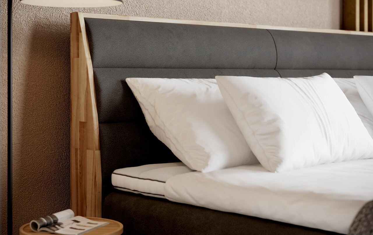 Close-up van een boxspringbed met een grijs hoofdeinde en witte kussens, gezien vanaf de zijkant