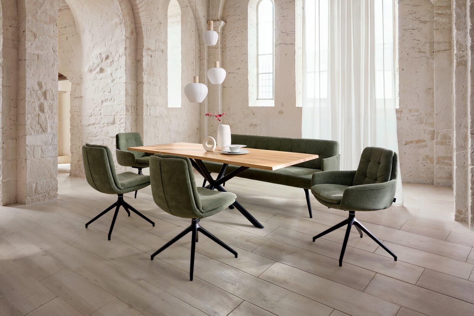 Dieter Knoll Esstisch TAVOLO Moderner Essbereich mit rechteckigem Holzesstisch, grüner Polsterbank und vier gepolsterten Drehstühlen mit schwarzem Metallfuß in hellem Loft mit Steinwänden, Seitenansicht in leichter Schrägperspektive von vorne rechts