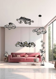 Moderne Wohnzimmeransicht mit mehreren Leuchten der Serie Nancy, darunter eine Stehleuchte, Pendelleuchten und eine Tischleuchte, in einem eleganten, geschwungenen Design mit Glasdetails.