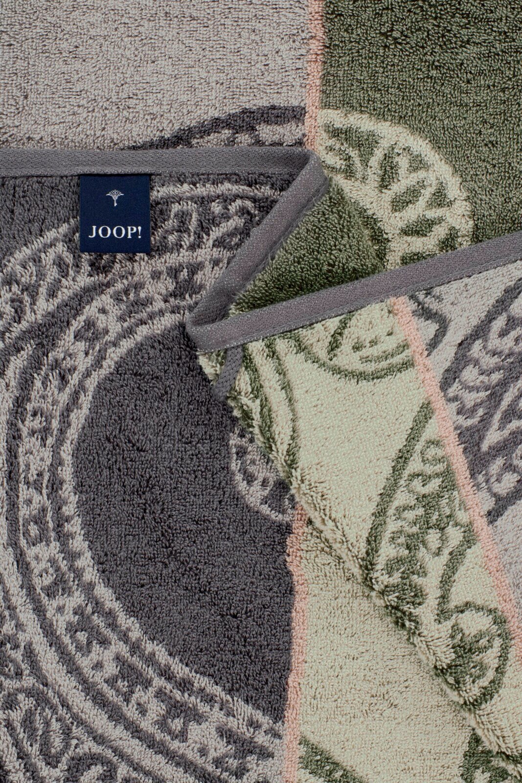 Detailaufnahme von JOOP! Frottierhandtüchern mit floralen Ornamenten in Grau, Grün und Beige, mit grauer Einfassung und sichtbarem Markenlabel, aus schräger Draufsicht