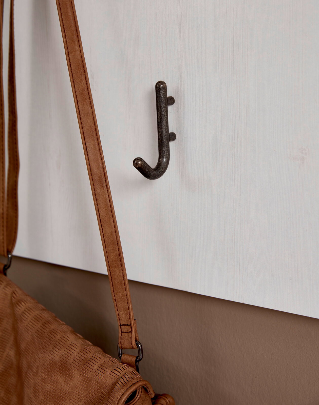 Nahaufnahme eines Garderobenpaneels mit einem Haken, an dem eine braune Tasche hängt. Perspektive von der Seite.