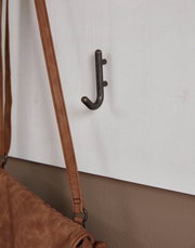 Nahaufnahme eines Garderobenpaneels mit einem Haken, an dem eine braune Tasche hängt. Perspektive von der Seite.