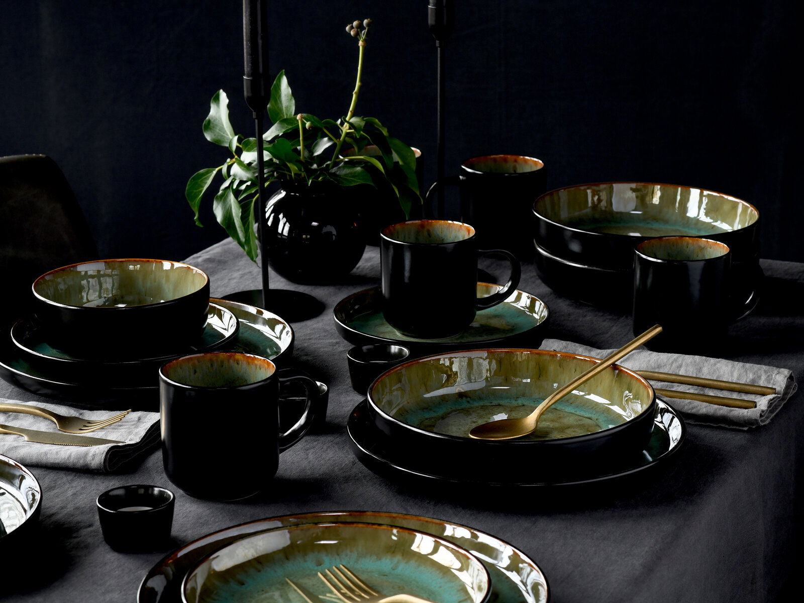 Elegantes Kombiservice 30-tlg. Green in Schwarz und Grün, auf einem gedeckten Tisch mit goldfarbenem Besteck und Pflanzen im Hintergrund, aus der Vogelperspektive fotografiert.