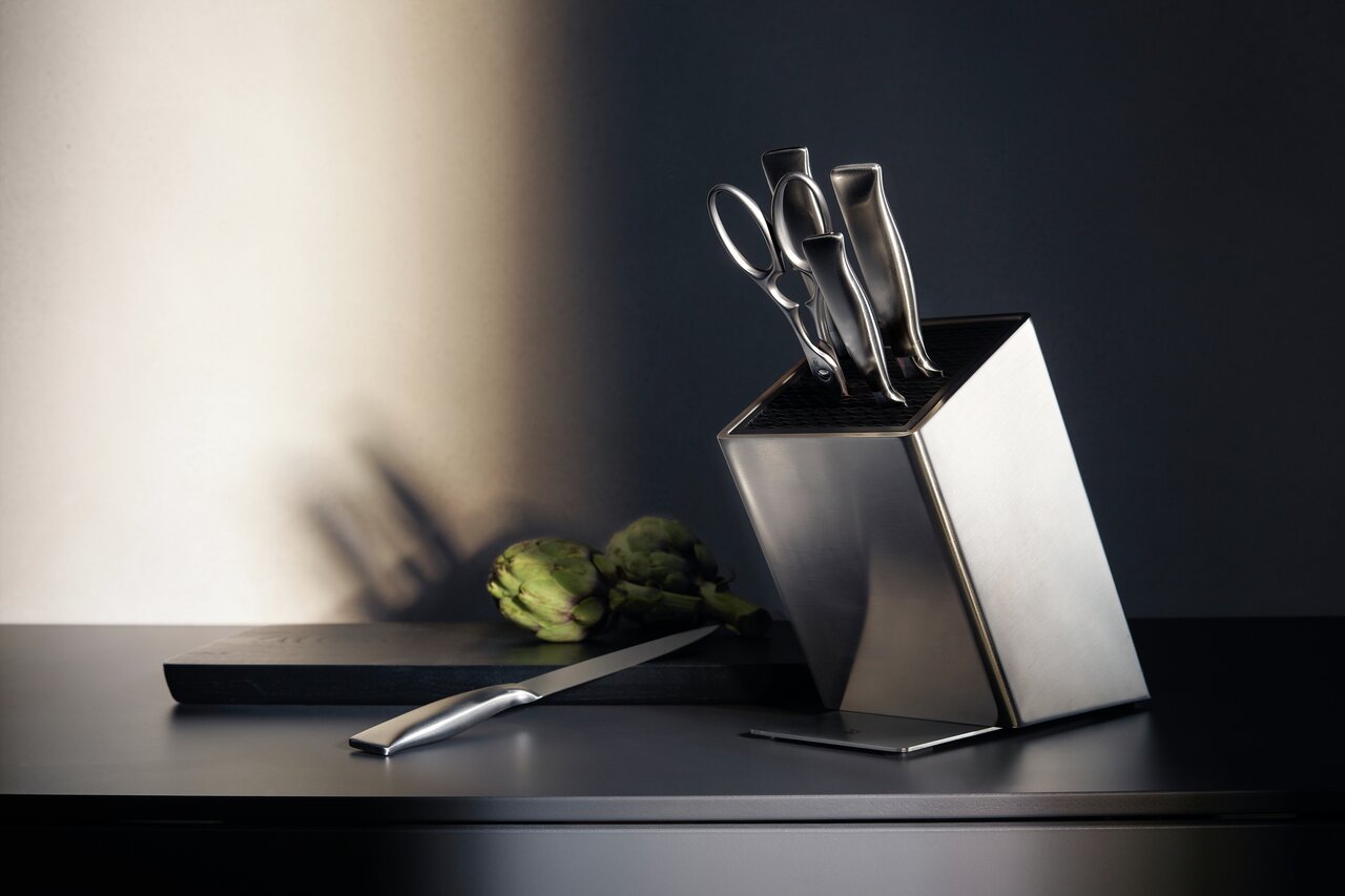 WMF Messerblock 6-tlg. GRAND GOURMET Moderner Messerblock aus Edelstahl mit fünf Messern und einer Schere, seitliche Perspektive, auf einer dunklen Arbeitsfläche mit einem Schneidebrett und einer Artischocke im Hintergrund.