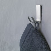 Seitliche Ansicht eines an der Wand befestigten, modernen Metallhakens mit einem daran hängenden dunkelblauen Handtuch.