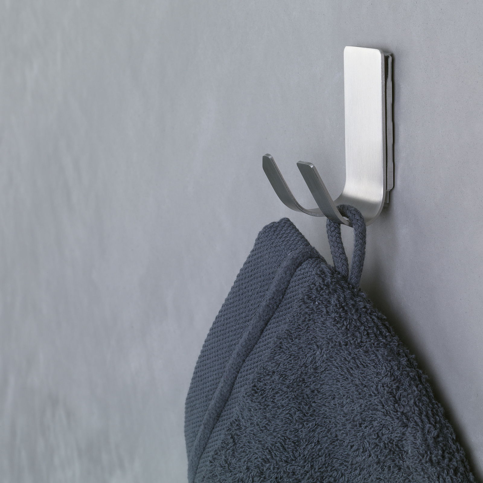 Seitliche Ansicht eines an der Wand befestigten, modernen Metallhakens mit einem daran hängenden dunkelblauen Handtuch.