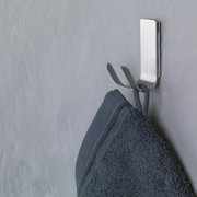 Seitliche Ansicht eines an der Wand befestigten, modernen Metallhakens mit einem daran hängenden dunkelblauen Handtuch.