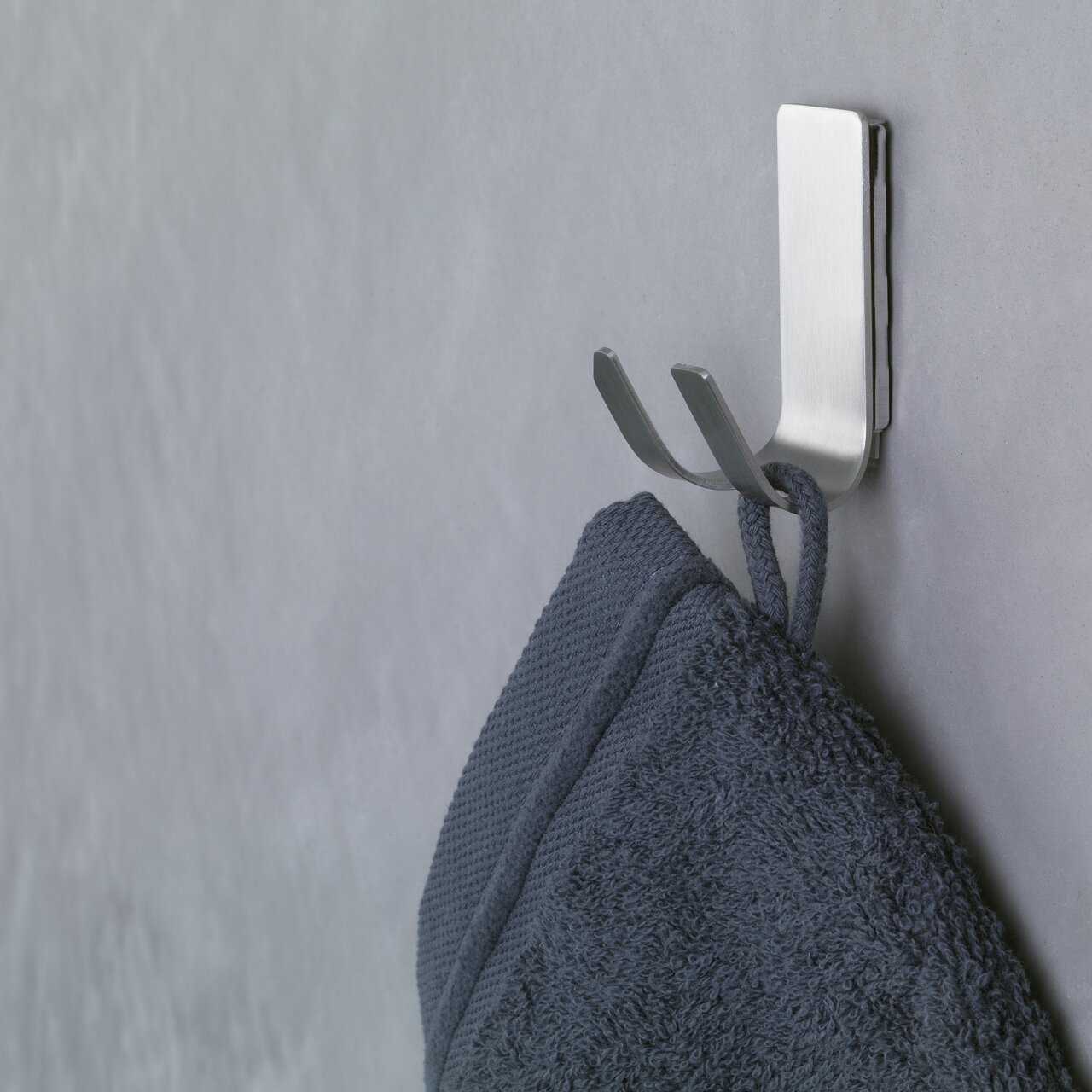 Seitliche Ansicht eines an der Wand befestigten, modernen Metallhakens mit einem daran hängenden dunkelblauen Handtuch.
