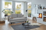 Graues Funktionssofa in modernem Wohnzimmer mit großen Fenstern, Pflanzen und Kamin, seitliche Perspektive.