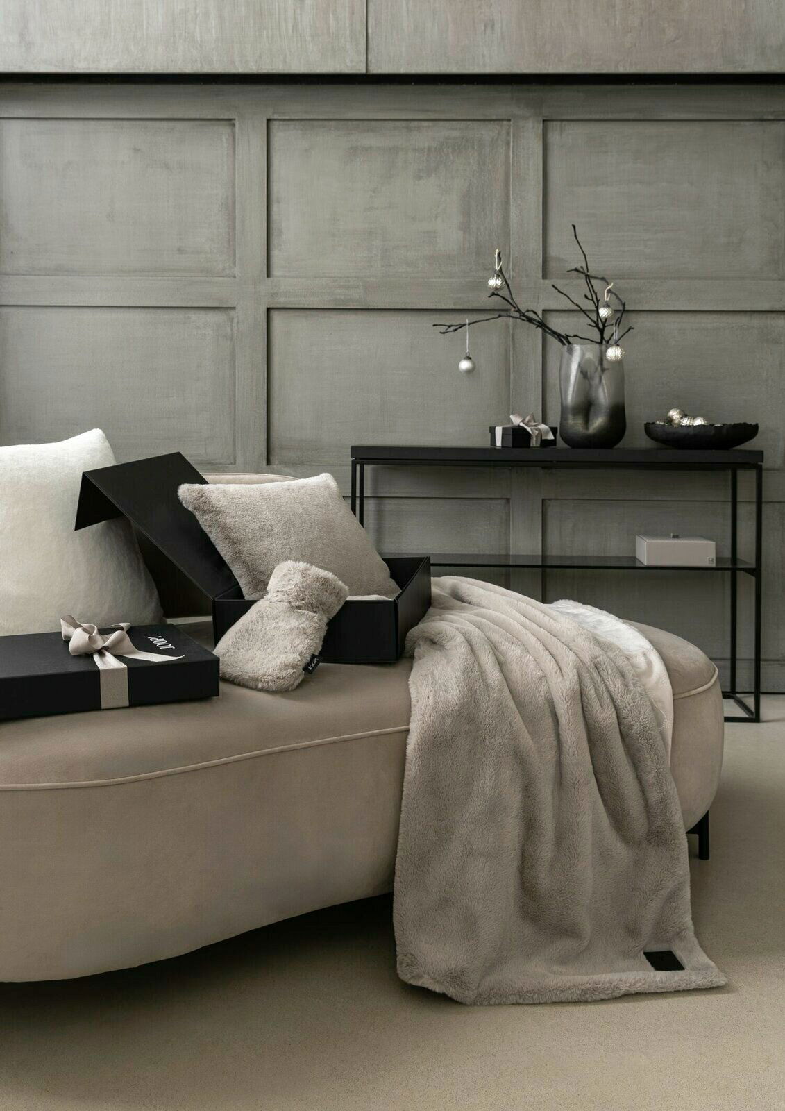 JOOP! Wohndecke J!CHALET Luxuriöse Wohndecke in Beige auf einem Sofa drapiert, mit passendem Kissen und Geschenkboxen, seitliche Perspektive.