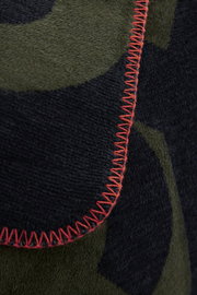 Nahaufnahme einer Jacquard-Decke mit grünem und schwarzem Muster und roter Ziernaht.