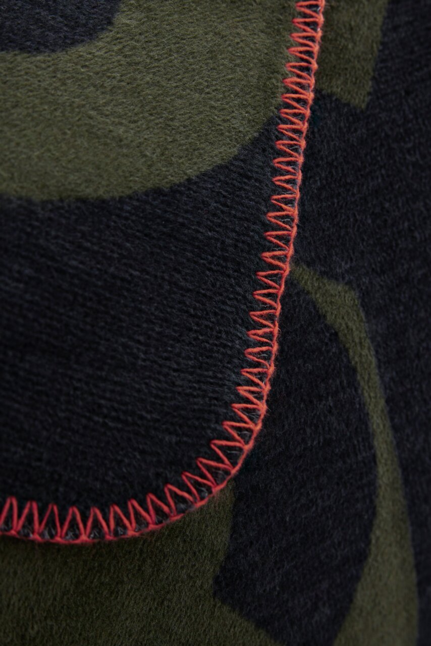 Nahaufnahme einer Jacquard-Decke mit grünem und schwarzem Muster und roter Ziernaht.