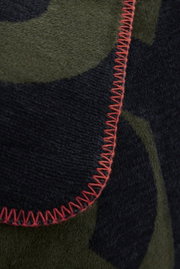 Close-up van een jacquarddeken met een groen en zwart patroon en een rode sierstik.